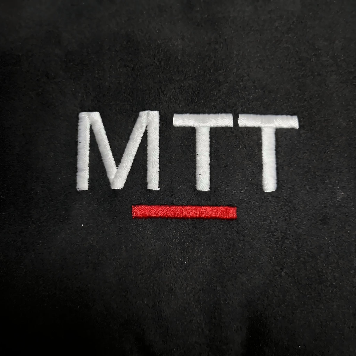 Kopfstützkissen: gestickte MTT-Wortmarke mit rotem Strich auf schwarzem Samt, Nahaufnahme